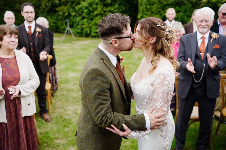 Bride and groom first kiss during outdoor ceremony at Pennard Hill Farm with guests applauding