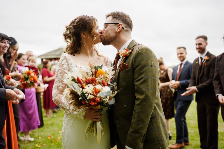 Newly married couple kissing outdoors surrounded by colorful confetti toss at Pennard Hill Farm