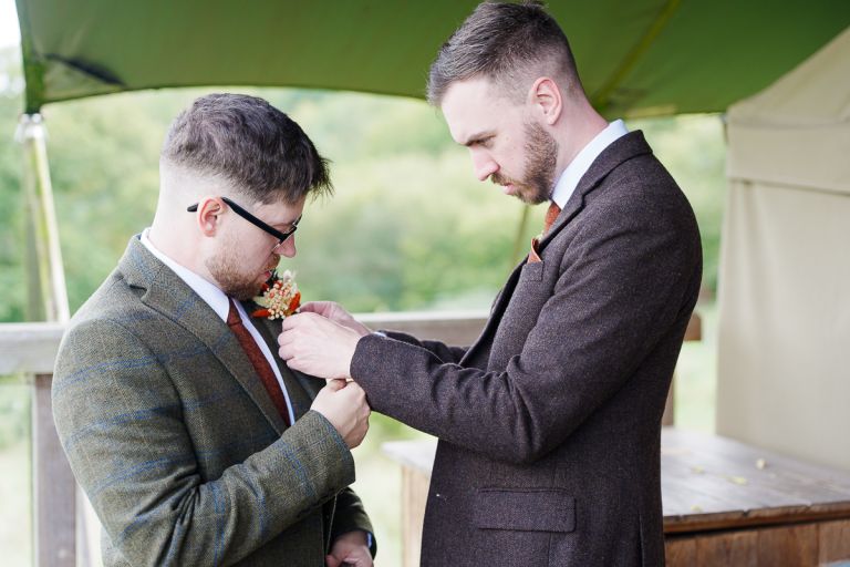 Groom having tweed suit buttonhole pinned during morning wedding preparations at Pennard Hill Farm