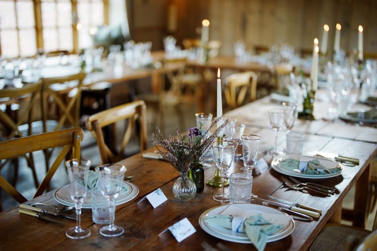Intimate feasting barn reception table setup with tall candles and rustic crossback chairs at Pennard Hill Farm