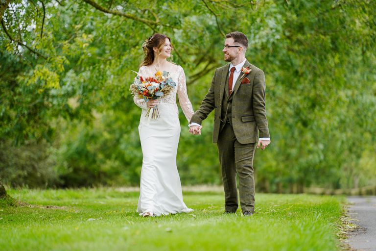 Bride and groom walking hand in hand across the green lawns at Pennard Hill Farm Somerset
